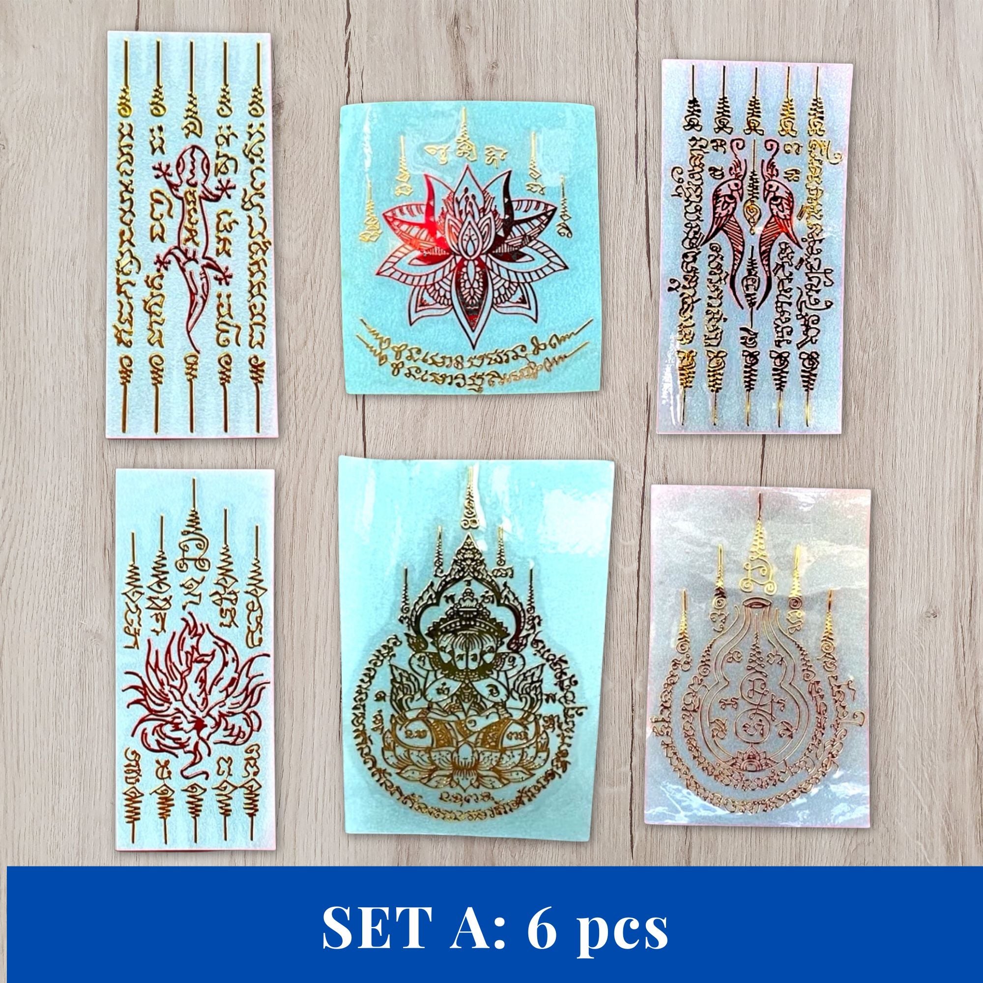 Six rectangular temporary tattoo sheets arranged in a 2x3 grid on a light wood surface, with a blue banner at the bottom reading 'SET A: 6 pcs'. The tattoos feature Thai-style script, floral motifs, and temple designs in metallic gold and red on pale blue, white, and clear sheets.